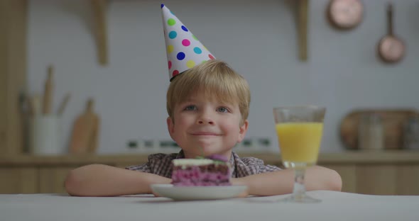 Portrait of Smiling Birthday Kid Sitting at the Table and Looking at Camera. Child in Birthday Hat