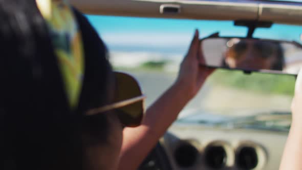 African american woman adjusting rear view mirror while sitting in the convertible car on road