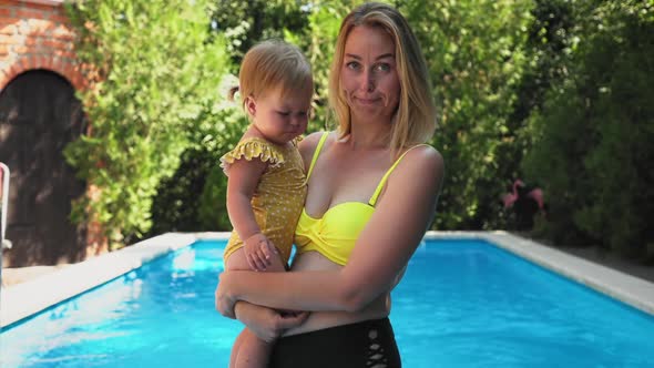 A nervous mother in a swimsuit holds a small crying child in her arms and calms him down