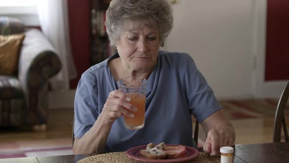 Elderly woman eating breakfast and taking pills.