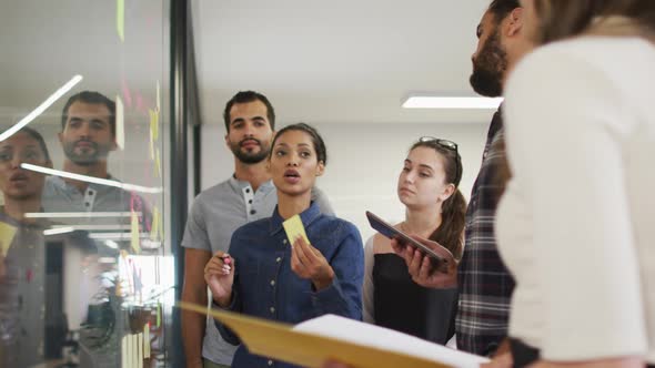 Diverse group of work colleagues brainstorming putting sticky notes on glass wall