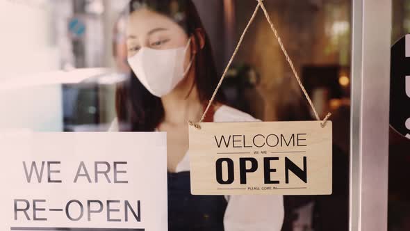 Business owner attractive young  asian woman in apron hanging we're open sign