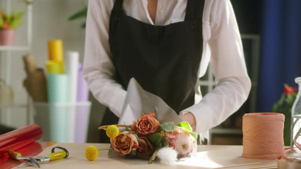 Young Florist Wrapping Bouquet of Roses and Dried Flowers Into Packaging Paper at Workplace