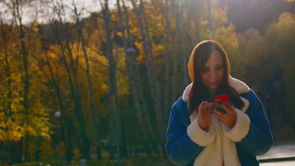 Young Woman Standing with Mobile Phone in City Park