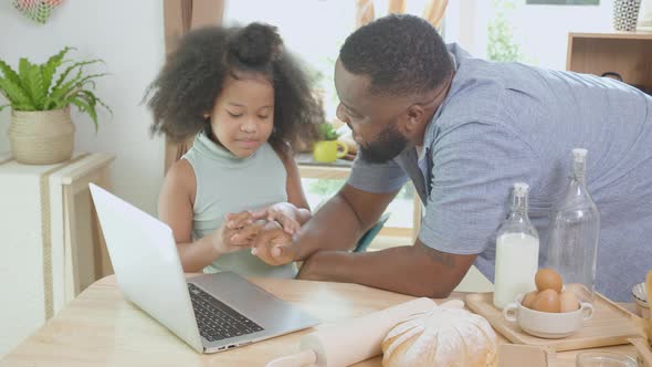 African America father and daughter learning recipe cooking online on laptop computer.