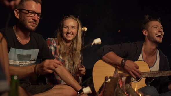 Young Caucasian Male Playing Guitar Laughing While Friends Sitting Around Listenning Talking Smiling