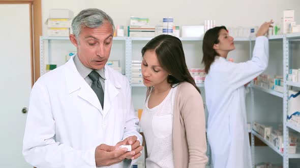 Pharmacist pointing at a flask of pills in front of a customer