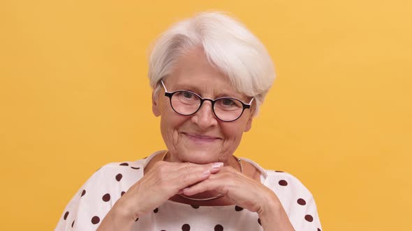 Serious Senior Woman Resting Head on Her Hands Starts To Smile. Isolated on the Orange Background
