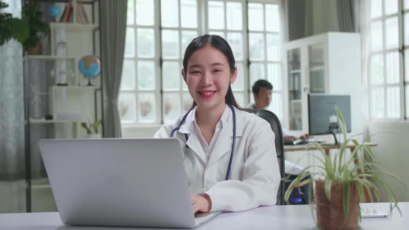 Young Asian Woman Doctor Is Using Laptop Computer And Smiling To Camera In Workplace