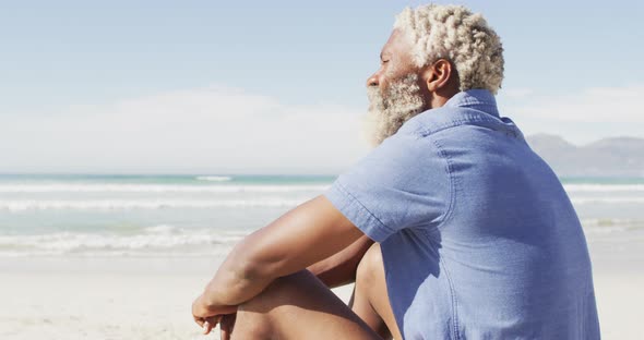 Senior african american man sitting and looking away on sunny beach