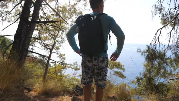 Male Hiker with Backpack Coming to Edge Hill and Admiring Beautiful Seascape