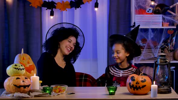 Mom and Daughter African American in Festive Costume and Witch Hat Having Fun and Eating Sweets