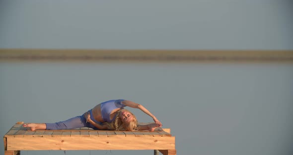Blonde Woman Wearing Blue Sportswear is Doing a Split Yoga Poses in the Lake