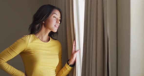 Curious biracial woman revealing curtains and looking outside window