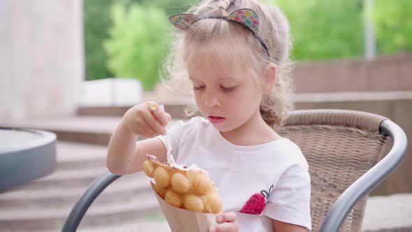 Little Girl Eat Bubble Waffle with Ice Cream Sitting Outdoor Cafe Summer Day