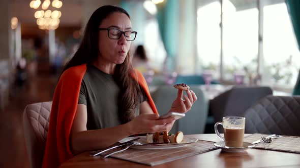 Middleaged Woman is Enjoying Lunch with Coffee in Restaurant and Using Smartphone