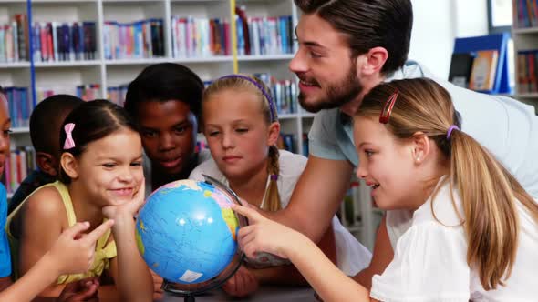 Teacher discussing globe with kids in library