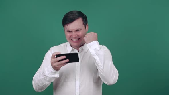 A young man with a smartphone in his hands rejoices in victory with a raised hand