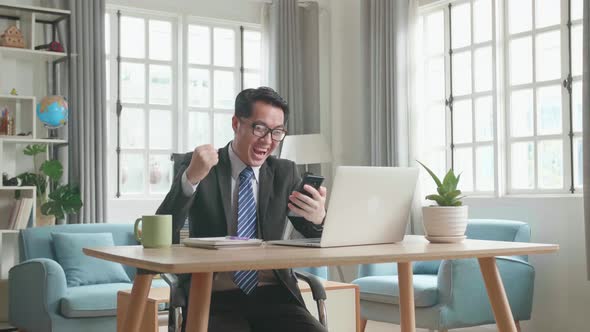 Happy Asian Businessman Looking At Mobile Phone While Working At Home