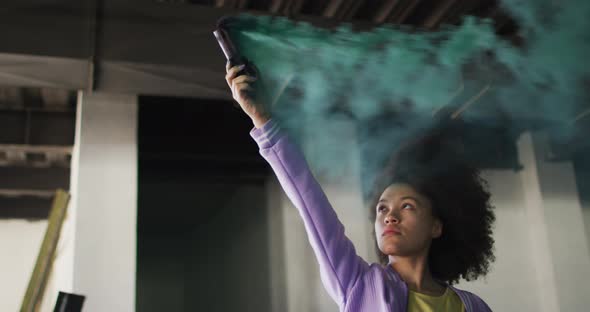 Mixed race woman holding green flare standing in an empty building