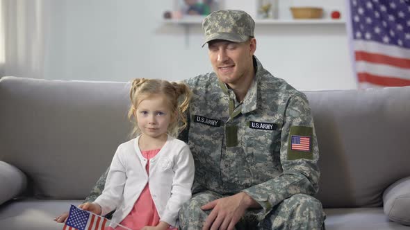 Happy US Soldier Admiring Daughter Waving National Flag, Sitting on Sofa at Home