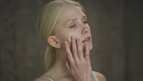 Closeup Beauty Portrait of Young Woman with Long Hair and Perfect Skin Applies Cream on Her Face