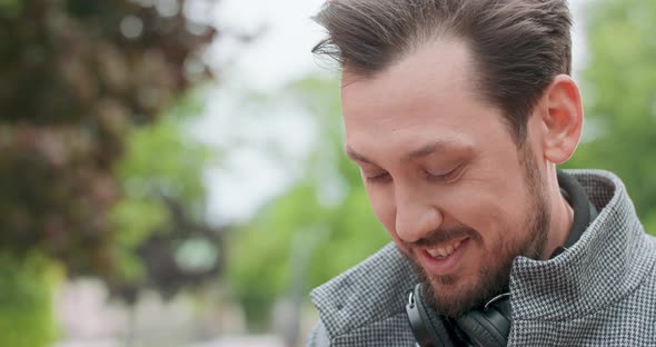 Young Man's Face with Mustaches and a Beard with Headphones on His Neck Who is Typing a Message on