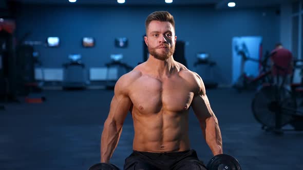 Fit young man lifting dumbbells doing workout at a gym. 