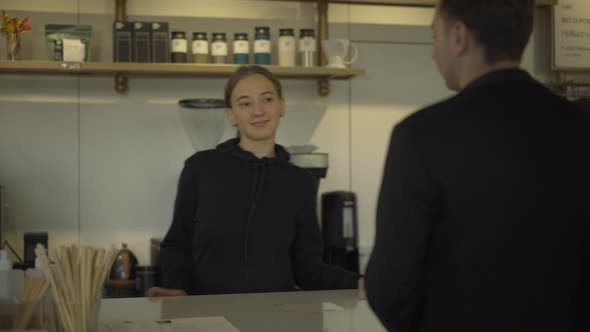 Portrait of Positive Caucasian Young Woman Receiving Order From Client in Cafe and Giving Man Two