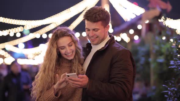 Happy couple having fun at amusement park and looking at mobile phone