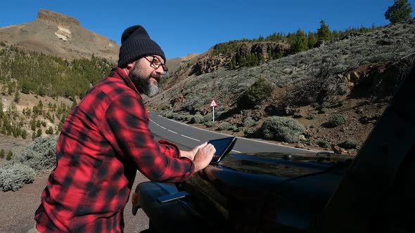 Traveler using digital tablet on car bonnet by country road