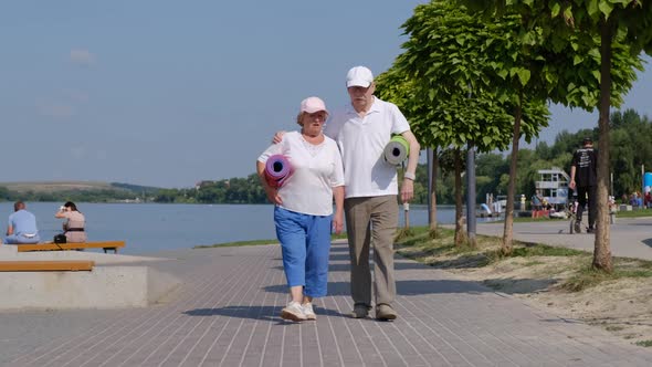 Lovely senior couple walking along the waterfront with yoga mats. Friendly atmosphere.