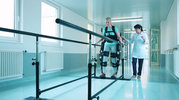 Doctor is Helping a Young Woman to Walk in the Exoskeleton