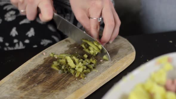 Woman with sharp knife chop pickle into small cubes on wooden board
