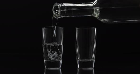 Pouring Up Two Shot of Vodka From a Bottle Into Glass. Black Background