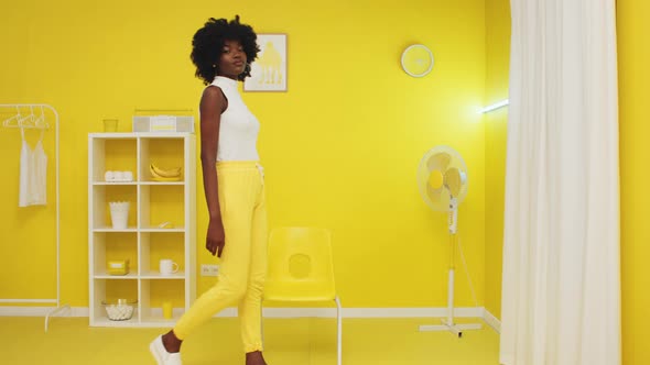 Black Woman Comes Into Shot and Sits On Yellow Chair