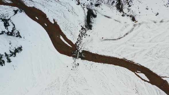 Drone Over Snowy Landscape With People Walking To Bridge Over River