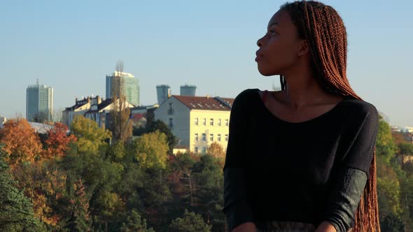 Young Beautiful Black Woman Looks Around in Park - Buildings in the Background