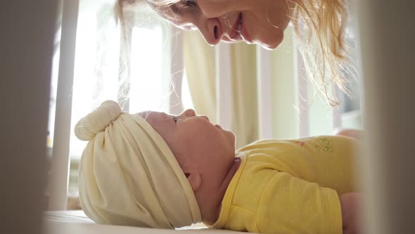 Joyful Young Mother Kisses Baby Girl in Yellow Clothing