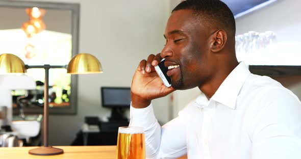 Man talking on mobile phone while having beer at counter