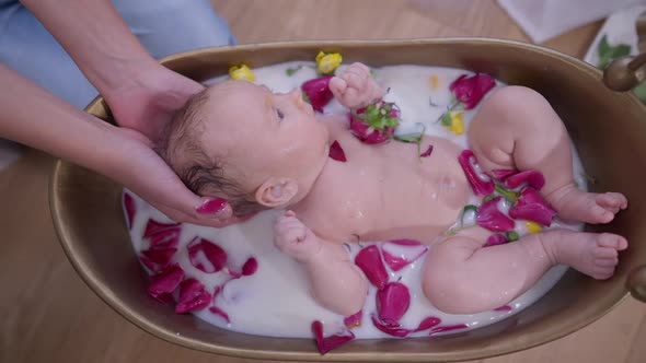 Top View Carefree Infant in Milk Water with Flower Petals and Male Teenage Hands Holding Head