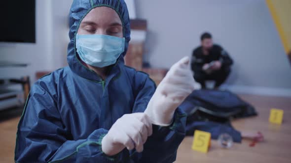 Portrait of Forensic Investigator in Uniform Putting on White Gloves and Looking at Camera