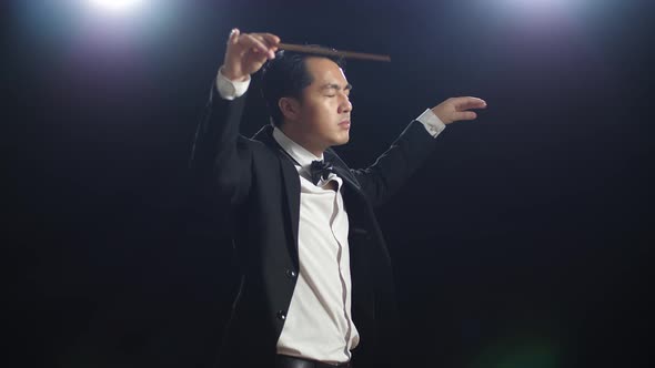 Side View Of Asian Conductor Man Holding A Baton Closing His Eyes And Showing Gesture