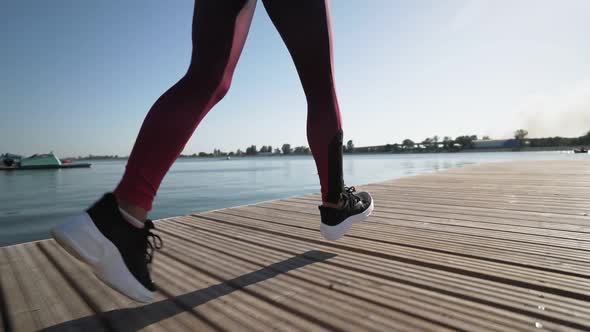 young athletic girl runs on pantone along the lake in black sneakers leggings