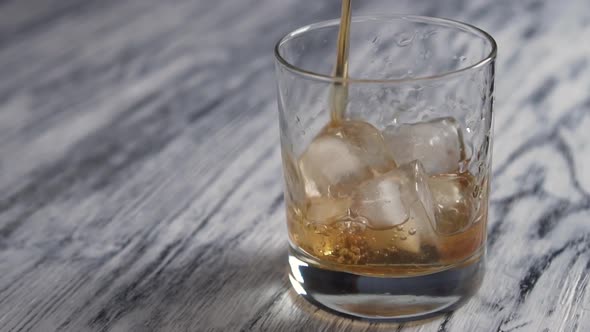 Golden whiskey is poured into a glass cup with ice cubes