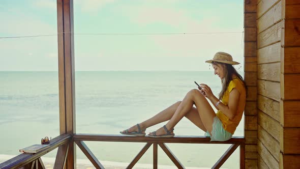 Side View Woman in Hat at Beach with Laptop Using Smartphone Online Chatting Browsing on Internet