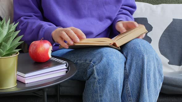 A woman eats an apple and reads a book in the garden.