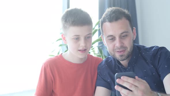 Dad and Son Look at the Smartphone and Smile