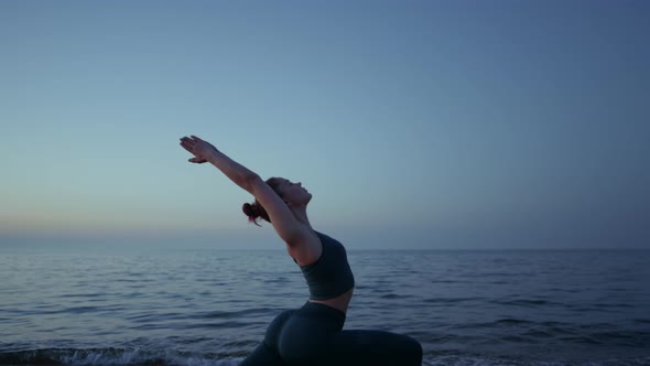 Flexible Girl Doing Warrior Asana Raising Hands to Sky