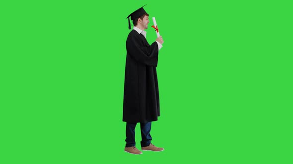 Smiling Male Student in Graduation Robe Posing with Diploma on a Green Screen Chroma Key